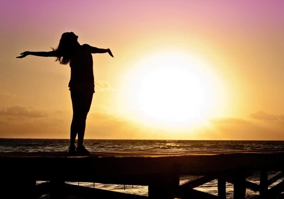 a woman standing arms outstretched toward the sunset symbolizing freedom from energy vampires